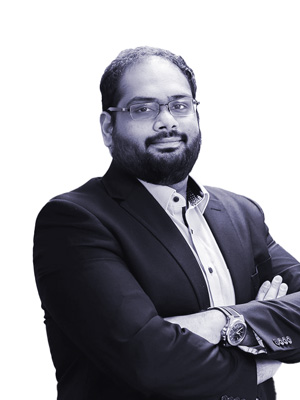 Karthik Balaji Director At Revenue Management Labs in a suit has his arms crossed and a watch on his wrist.